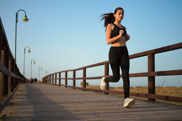 Young woman jogging on a wooden boardwalk at dusk