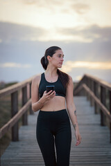 Young woman checking her phone on a wooden boardwalk at dusk