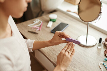 Closeup of unrecognizable young woman doing manicure at home and using nail file copy space