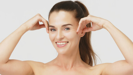 Naklejka premium Happy mature middle-aged woman touching face and looking at camera. Healthy, dry skin care concept, cosmetics and anti-aging plastic surgery.