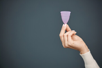 Minimal close up shot of female hand holding pink menstrual cup on dark blue background copy space