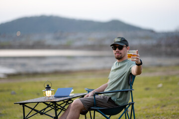 A relaxed man enjoys a peaceful moment sipping tea by a serene lakeside as the evening sets in.