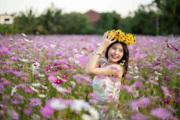 Fototapeta premium Young woman with floral crown smelling flowers in a vibrant field during sunset.