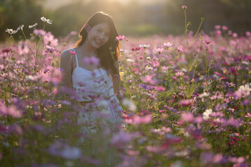 Young woman with floral crown smelling flowers in a vibrant field during sunset.