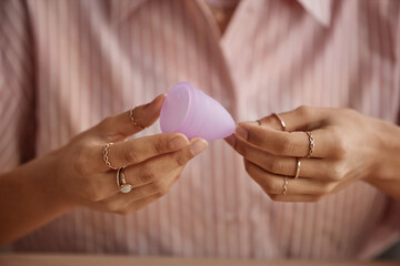 Minimal close up of unrecognizable woman holding pink menstrual cup against pink shirt copy space - obrazy, fototapety, plakaty