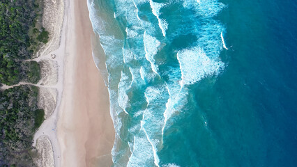 Fototapeta na wymiar Foamy ocean waves roll and approach sandy beach. Majesty turquoise seascape. Top view from a drone.