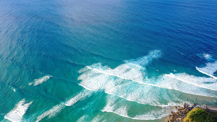 Patterned foamy ocean waves roll in and approach sandy beach. Majesty turquoise sea. Top view drone.