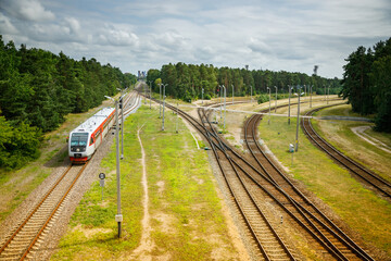 A modern passenger train moving along a railway track amidst a green landscape, in Klaipeda, Lithuania