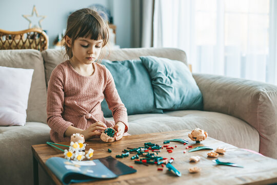 A sweet little girl crafting with small colorful construction pieces on a wooden table, sitting in a cozy living-room