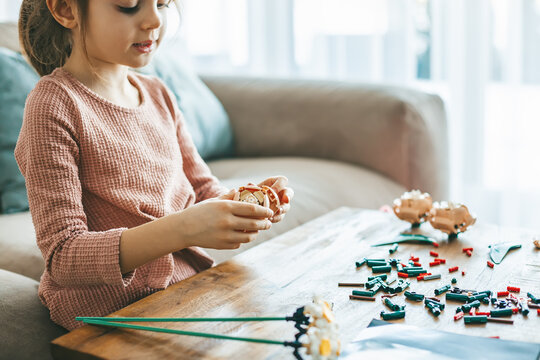 A delightful little girl is occupied with small colorful construction pieces, sitting on a couch in a living-room