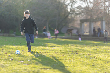 A boy is playing soccer in a park
