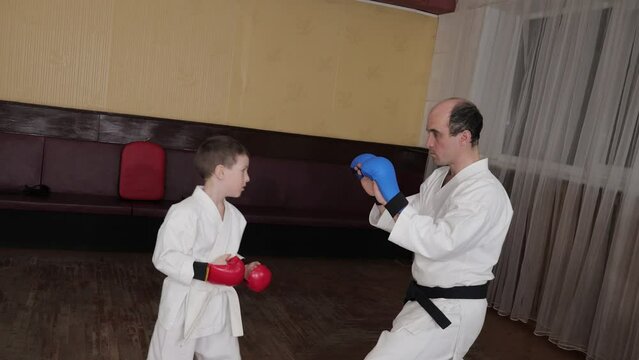 A coach trains a little athlete in red pads to perform punches