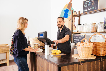 Smiling Woman Checking Out at a Small Grocery Store Counter With a Friendly Cashier