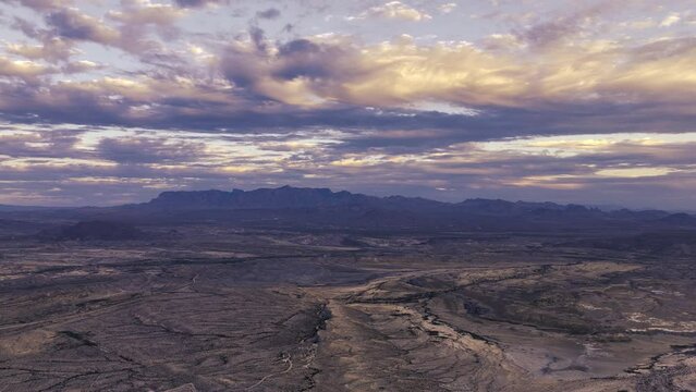 Cinematic Sunset timelapse over Chisos mountain range aerial view with dramatic lighting and moving cloudscape over vast West Texas desert in Big Bend