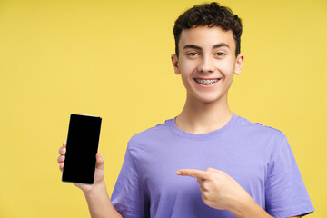 Teenager with braces, holding mobile phone, using mobile app, pointing finger at empty screen