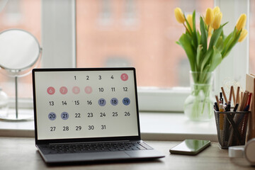 Background image of laptop computer with calendar on screen at workplace table by window with flowers, copy space