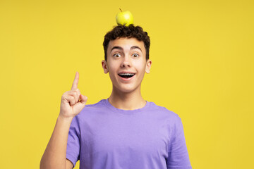 Smiling excited boy, teenager holding apple on head, finger up, having idea looking at camera