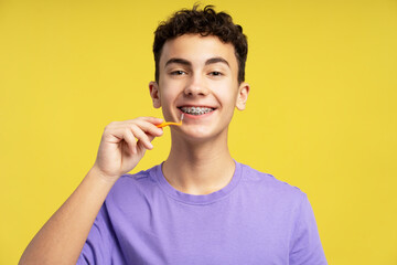 Happy boy with braces using interdental brush, looking at camera. Attractive teenager patient