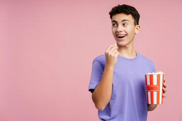 Smiling attractive teenager eating popcorn, holding bucket looking away at copy space