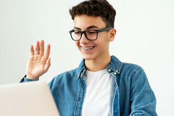 Smiling boy teenager, student with braces wearing stylish eyeglasses and casual clothes waving hand