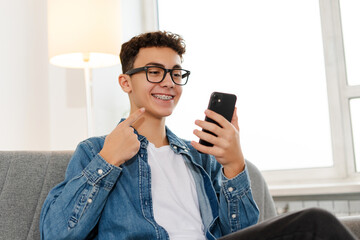 Attractive smiling boy, teenager with braces wearing stylish eyeglasses, holding mobile phone