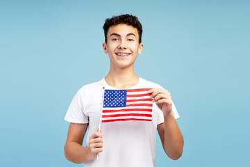 Handsome teenage boy, supporter with braces holding American flag pointing, looking at camera