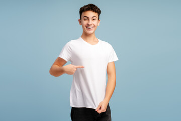 Happy, excited boy wearing white t shirt, pointing finger at her, mockup, looking at camera