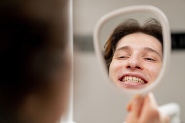 close up dental office a young guy sits in chair and looks at his teeth through a dental mirror