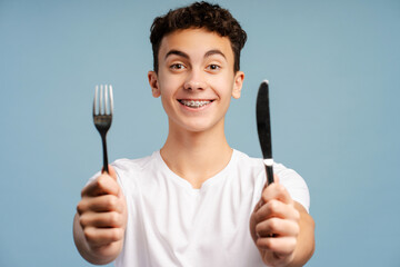 Handsome attractive boy holding fork and knife looking at camera