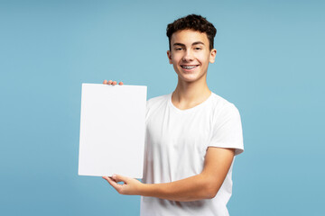 Confident handsome boy with braces holding white blank screen looking at camera