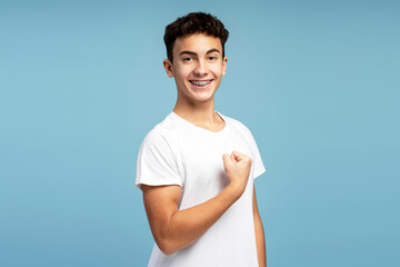 Portrait of happy strong teenage boy wearing stylish white t shirt showing muscles looking at camera