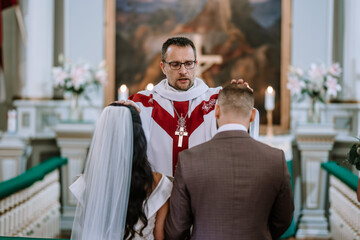 Valmiera, Latvia- July 28, 2024 - A priest with a stole blesses a bride and groom during their wedding ceremony in a church. - obrazy, fototapety, plakaty