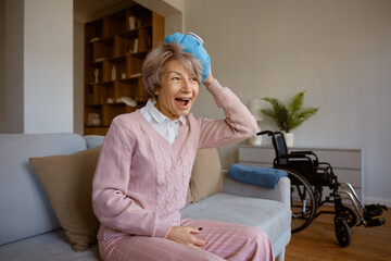 Super excited senior woman holding ice bag on head resting after injury - 787133262