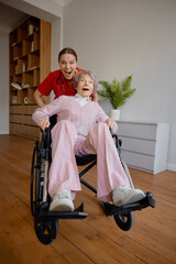 Crazy woman caregiver riding fast elderly woman patient on wheelchair - obrazy, fototapety, plakaty