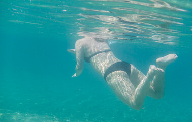 young woman in black bikini snorkeling in clear sea water on vacation