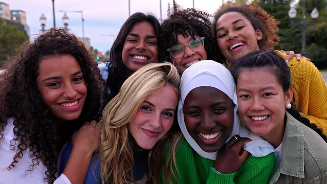 United portrait of young multiracial girls smiling at camera standing together outdoors. Millennial female friends feeling hugging each other smiling and posing for a photo. Women community concept.