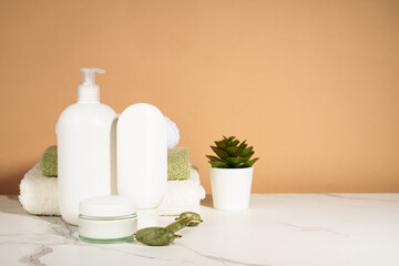 Skin care products in the bathroom. Face cream, serum bottle, jade roller and stack of towels. - 787143244