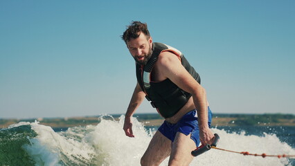 A man learns to wakesurf behind a boat. Fun on the water during the hot summer on the lake.
