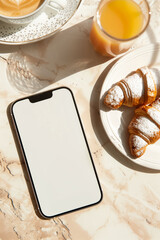 Smartphone Mockup on Marble Table with Breakfast: Top View of Modern Mobile Phone with White Screen Mockup next to Cappuccino Coffee, Orange Juice and Croissants