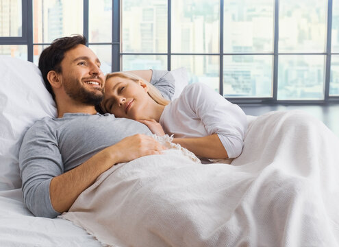 Sleeping couple. Woman, bearded man lay on home bed in bedroom room against big windows  background- love, relationship, dating, happy family, comfortable, waiting child concept image.