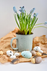 Easter eggs and light blue muscari flowers in cup on a brown kraft paper background on a white table. Easter still life.