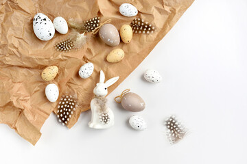 Easter composition with white rabbit, eggs and feathers on a brown kraft paper background on a white table. Top view. For easter greeting cards with copy space.