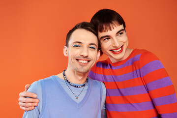 Obraz premium merry attractive gay friends with vivid makeup posing together on orange backdrop, pride month