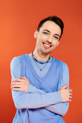 Obraz premium positive attractive stylish gay man with vibrant makeup posing on orange backdrop, pride month