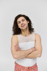 cheerful appealing gay man with long hair in casual attire smiling at camera on gray backdrop