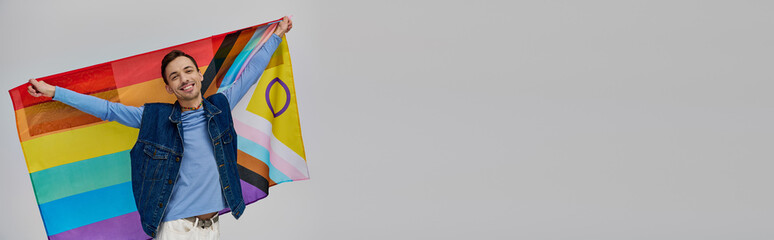 jolly appealing gay man in vibrant casual attire holding rainbow flag and smiling at camera, banner © Bliss