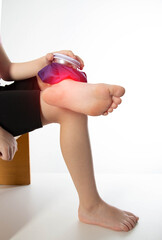A girl applies a blue medical bag with ice to her ankle joint for a bruise on her leg. Local...