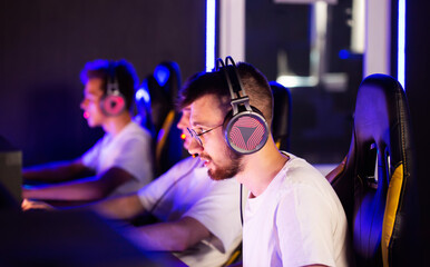 Bristly adult gamer in headset playing PC video game at computer club with team cyber sport tournament. E-sport championship. 5 player in headphones. Multiplayer online real-time strategy shooter - 787160868