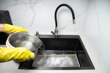 Man's hands in yellow gloves pour pots of hot water into a sink with dirty filters from the hood in the kitchen. Cleaning from dirt and grease with an oxygen cleaner. Copy space for text - 787161214