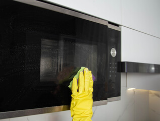 A girl's hand in a yellow glove with a sponge washes the microwave oven from grease and dirt. Foam and anti-grease. Cleaning household appliances in the kitchen - 787161229